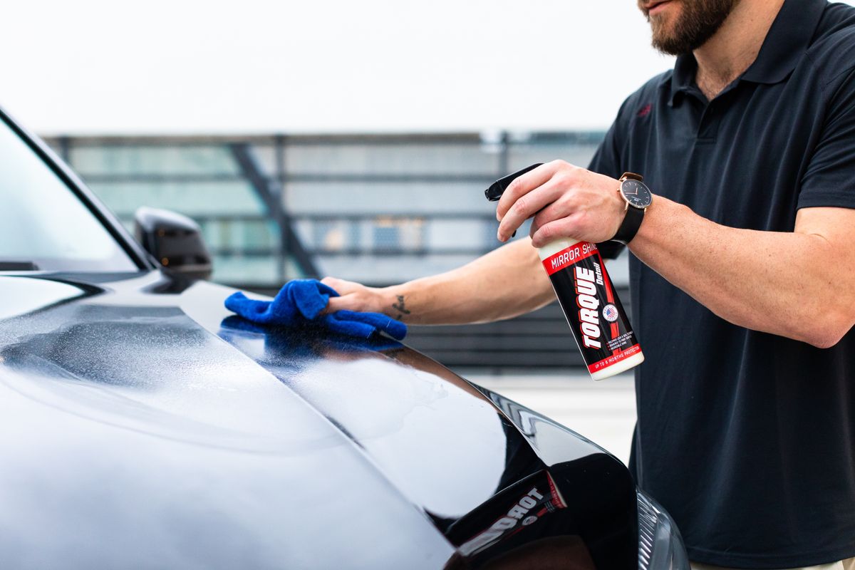 A cloth and detailing spray cleaning a dark car bonnet